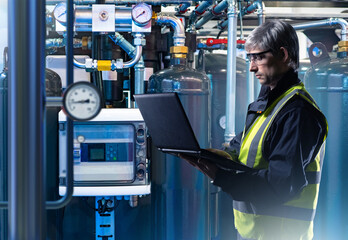 Poster - Man engineer. Factory technologist holding laptop. Engineer indoors with pipes and sensors. Factory worker inspects gas equipment. Man technologist in reflective vest. Inspector controls work factory