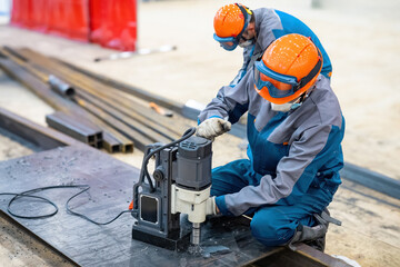 Man worker with magnetic drilling machine. Builder drills hole in metal sheet. Using magnetic drilling machine during construction. Creating holes in thick iron sheet. Industrial drilling machine