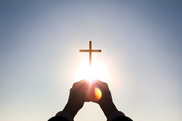 Wall Mural - Brightly shining sunlight and silhouette of Christian hands holding high the cross of Jesus Christ symbolizing death and resurrection
