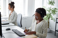 Two Women Sitting At Desk In Office And Talking Via Headset