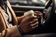 Close-up of African American man's hands holding steering wheel and cardboard cup of coffee in car