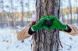 Nature lover hugging trunk tree with green mittens in winter woods forest. Natural background. Concept of people love nature and protect from deforestation or pollution or climate change.