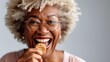 Joyful elderly lady enjoys a cookie against a studio backdrop.