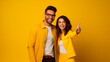 pareja feliz de latinos señalando en un fondo amarillo 