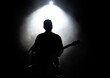 Musician playing guitar performing on stage under spot light. Silhouette of a music artist and band on stage.