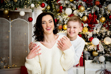 Wall Mural - smiling happy mother and child wearing white sweaters sitting  near  christmas tree 