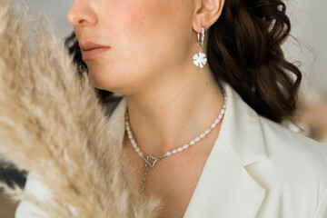 Wall Mural - Close up of beautiful elegant young woman wearing an expensive pearl necklace and earrings in a white blazer