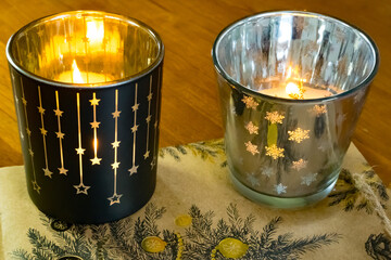 christmas candle in a glass: Two lanterns in festive decor with burning candles on Christmas wrapping paper.