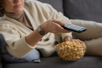 Wall Mural - Close-up of young woman lying on sofa and using remote control to watch TV with popcorn