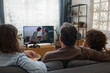 © Mediaphotos - Rear view of family watching TV together in the living room while resting on sofa