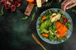 delicious winter salad with persimmon, fresh greens, avocado, Camembert cheese and pomegranate on a dark background. top view. copy space for text