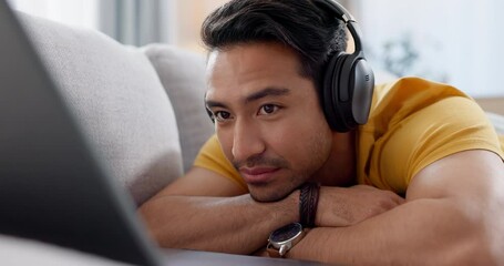 Poster - Asian man, laptop and relax on sofa with headphones for entertainment or online streaming at home. Happy male person smile and lying on living room couch watching on computer with headset at house