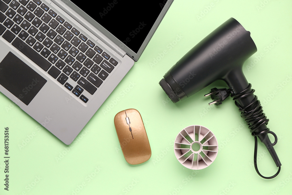 Laptop with computer mouse and hair dryer on green background