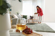 Beautiful young Asian woman with glass of wine, grapes and snacks in living room