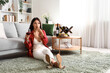 Beautiful young Asian woman with glass of wine eating grapes in living room