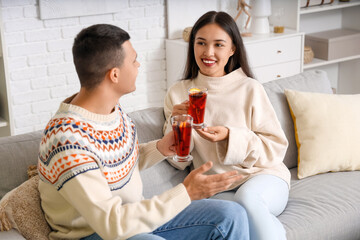 Wall Mural - Happy couple with glasses of warm mulled wine sitting on sofa in living room