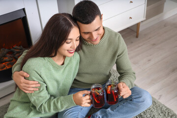 Sticker - Happy couple with glasses of warm mulled wine sitting on floor in living room