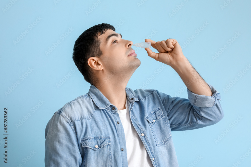 Young man using nasal drops on blue background