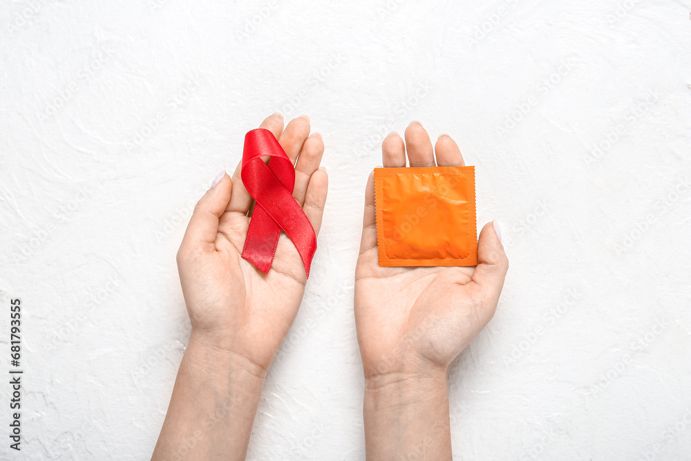 Female hands with red ribbon and condom on white grunge background. AIDS Day concept