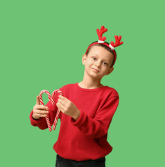 Sticker - Cute little boy in reindeer horns with candy canes on green background