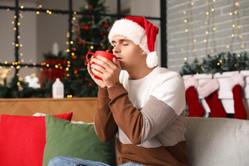 Wall Mural - Young man drinking hot cocoa at home on Christmas eve