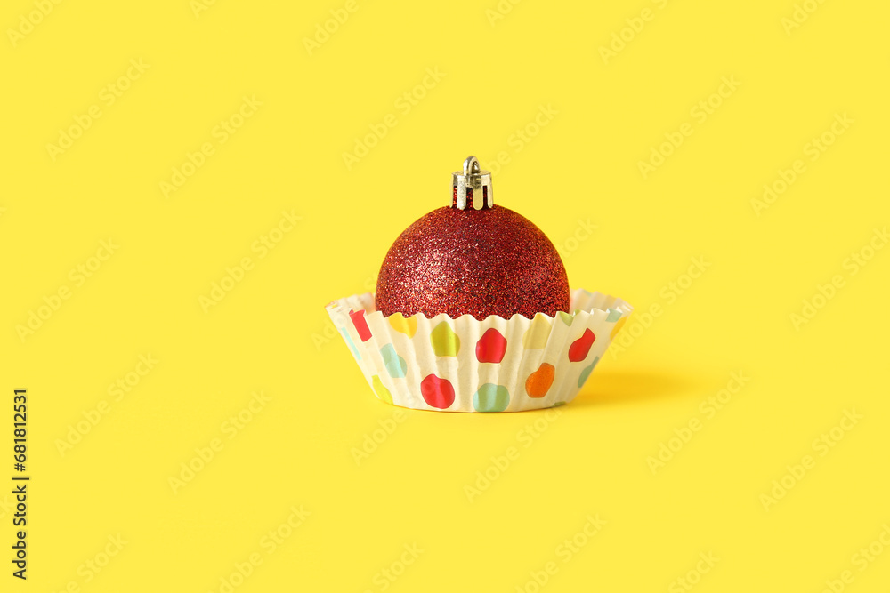 Muffin baking cup with beautiful Christmas ball on yellow background