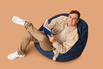 Wall Mural - Young man lying on beanbag and reading book against color background