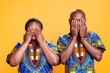African american couple covering eyes with arms, showing hear no evil three wise monkeys portrait. Black man and woman pair holding palms on face on orange studio background