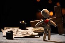 Voodoo Doll Pierced With Pins And Ceremonial Items On Wooden Table Against Blurred Background