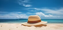 A Stylish, Wide-brimmed Sun Hat Resting On A Tropical Beach, With A Background Of Azure Ocean Waters And A Clear, Bright Sky. The Hat Casts A Delicate Shadow On The Smooth Sand.