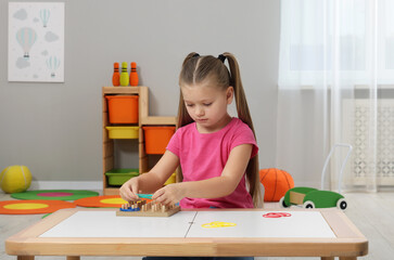 Wall Mural - Motor skills development. Girl playing with geoboard and rubber bands at white table in kindergarten