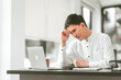© Ratirath - Asian male people concerned person in white shirt looks at laptop, possibly stressed, hand on their forehead. middle age businessman