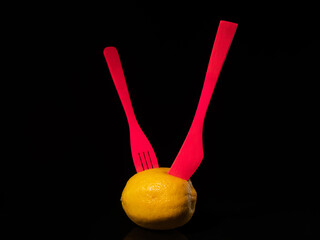 Wall Mural - Composition with lemon, knife and fork on a black background