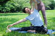 © Monet - Asian man in sportswear stretching on a yoga mat on the grass, assisted by a woman.