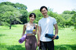 Portrait of a young male and female couple laughing while holding yoga mats and water in a lush park.