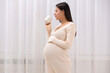 © New Africa - Beautiful pregnant woman with cup of drink indoors