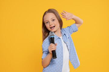 Cute little girl with microphone singing on yellow background