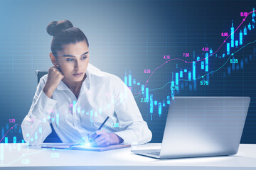 Wall Mural - Attractive young businesswoman working at desk with laptop and glowing upward candlestick forex chart on blurry grid background. Trade, finance and money concept.