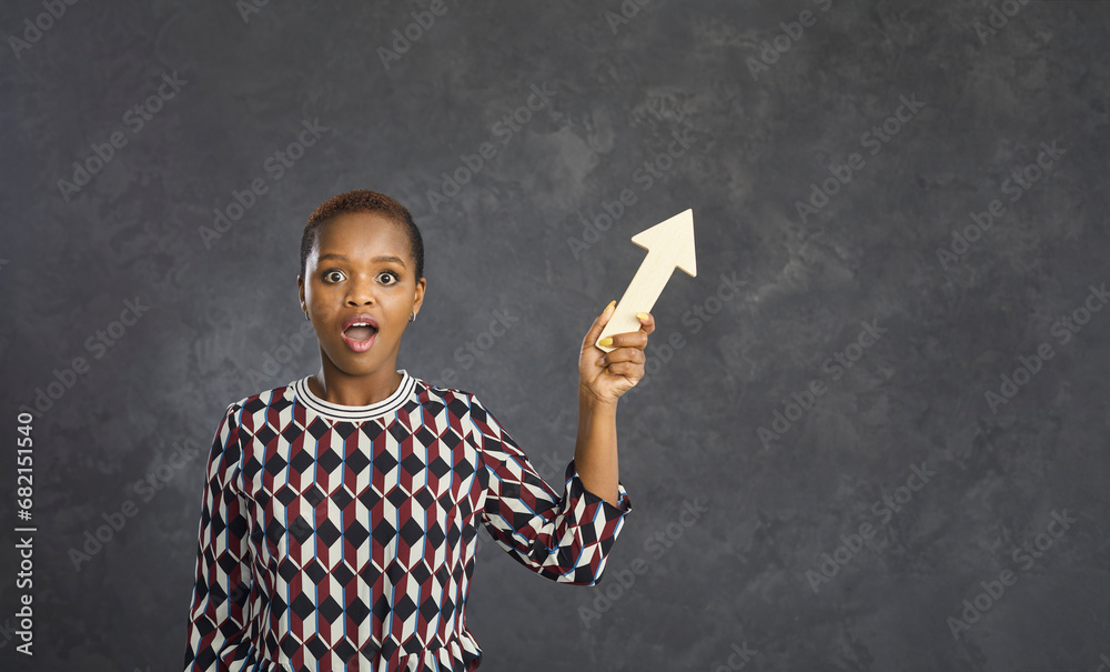 Shocked young african american woman pointing a wooden arrow away while ...