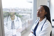 © WavebreakMediaMicro - Thoughtful african american female doctor wearing lab coat looking through window in hospital room