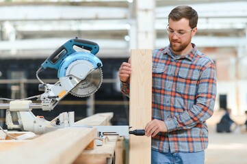 Wall Mural - A carpenter works on woodworking the machine tool. Man collects furniture boxes. Saws furniture details with a circular saw. Process of sawing parts in parts. Against the background of the workshop.