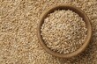 Pearl barley in bowl on dry grains, top view. Space for text