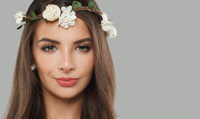 Spring fashion model with dark healthy hairstyle, fresh clean skin, trendy make-up and flower wreath looking at camera on gray background. Brunette woman portrait