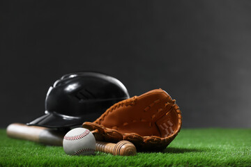 Wall Mural - Baseball bat, batting helmet, leather glove and ball on green grass against dark background. Space for text