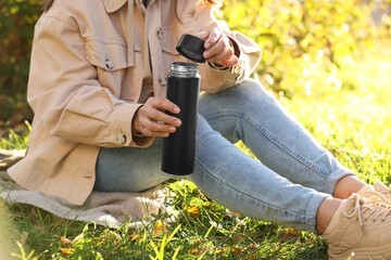 Poster - Woman opening thermos on green grass outdoors, closeup