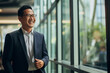 © Surachetsh - The portrait of an Asian mature businessman in a tidy suit with glasses smiles and stands confidently in the hallway of a modern company. Generative AI.