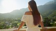 © Кирилл Рыжов - A young brunette woman, dressed in a flowing dress, stands on the villa terrace or balcony, enjoying mountain sunset. Summertime, mountain bliss, holiday serenity, and travel