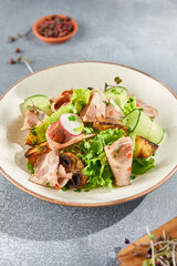 Canvas Print - A vertical presentation of a nutritious salad with baked meat and fresh vegetables. The ceramic plate sits on a minimalist gray concrete background