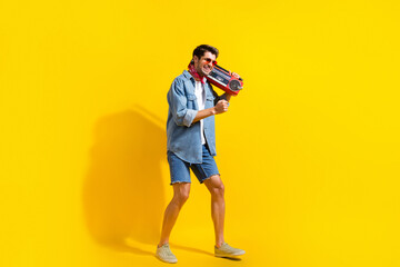 Poster - Full size photo of funny guy wear jeans jacket shorts in sunglass hold boombox look empty space isolated on yellow color background