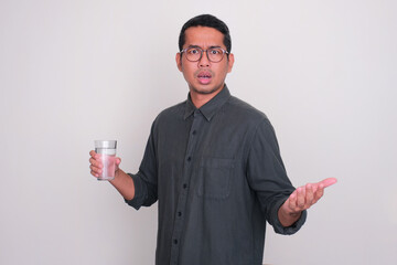 Wall Mural - Adult Asian man holding a glass of water with worried expression